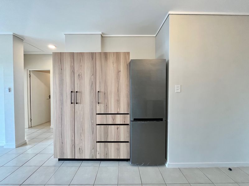A clean kitchen area featuring modern wood-finish built-in cabinetry and light-colored floor tiles, providing a functional and neutral storage space.