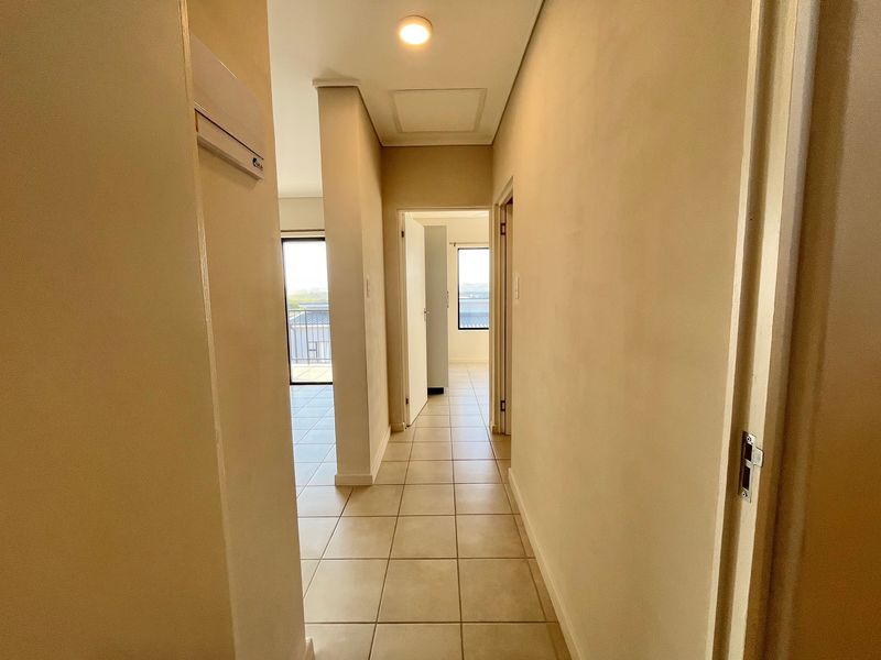 A clean, neutral-toned hallway featuring tiled flooring, recessed lighting, and an integrated air conditioning unit, providing access to adjacent rooms.
