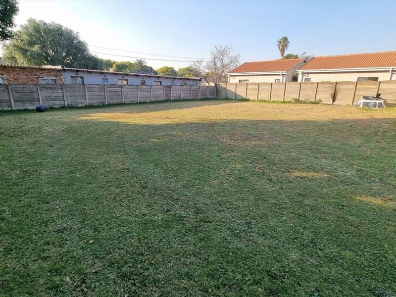 A spacious, level backyard featuring a large lawn area enclosed by precast concrete boundary walls, offering potential for landscaping or outdoor development.