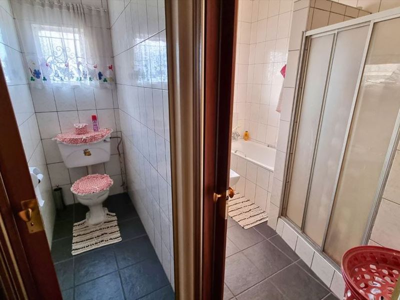 A functional bathroom featuring a separate toilet area, bathtub, and a glass-enclosed shower with tiled finishes throughout.