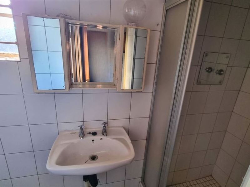 A dated bathroom featuring a wall-mounted basin, shower enclosure, and tiled walls, requiring modernization to improve its overall condition and appeal.