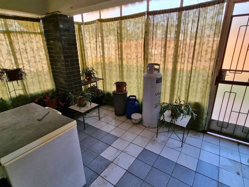 An enclosed patio area featuring tiled flooring, a brick pillar, and a security gate, offering a versatile space for outdoor living.