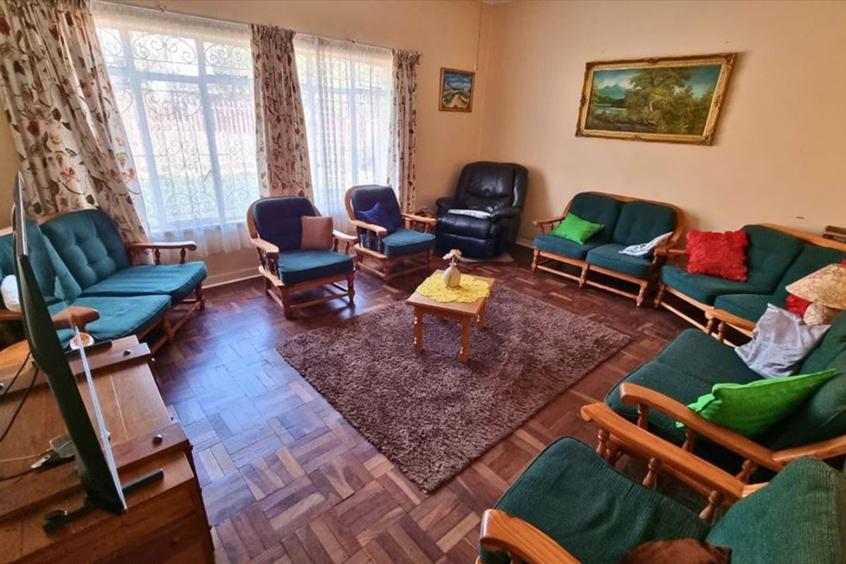 A traditional living room featuring classic parquet flooring and large windows fitted with security bars, offering a functional and well-lit space.