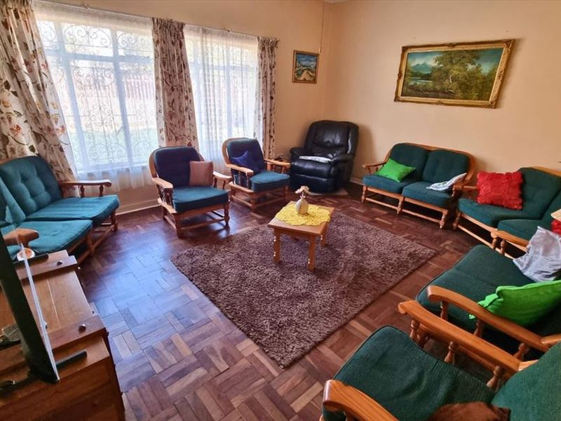 A traditional living room featuring classic parquet flooring and large windows fitted with security bars, offering a functional and well-lit space.