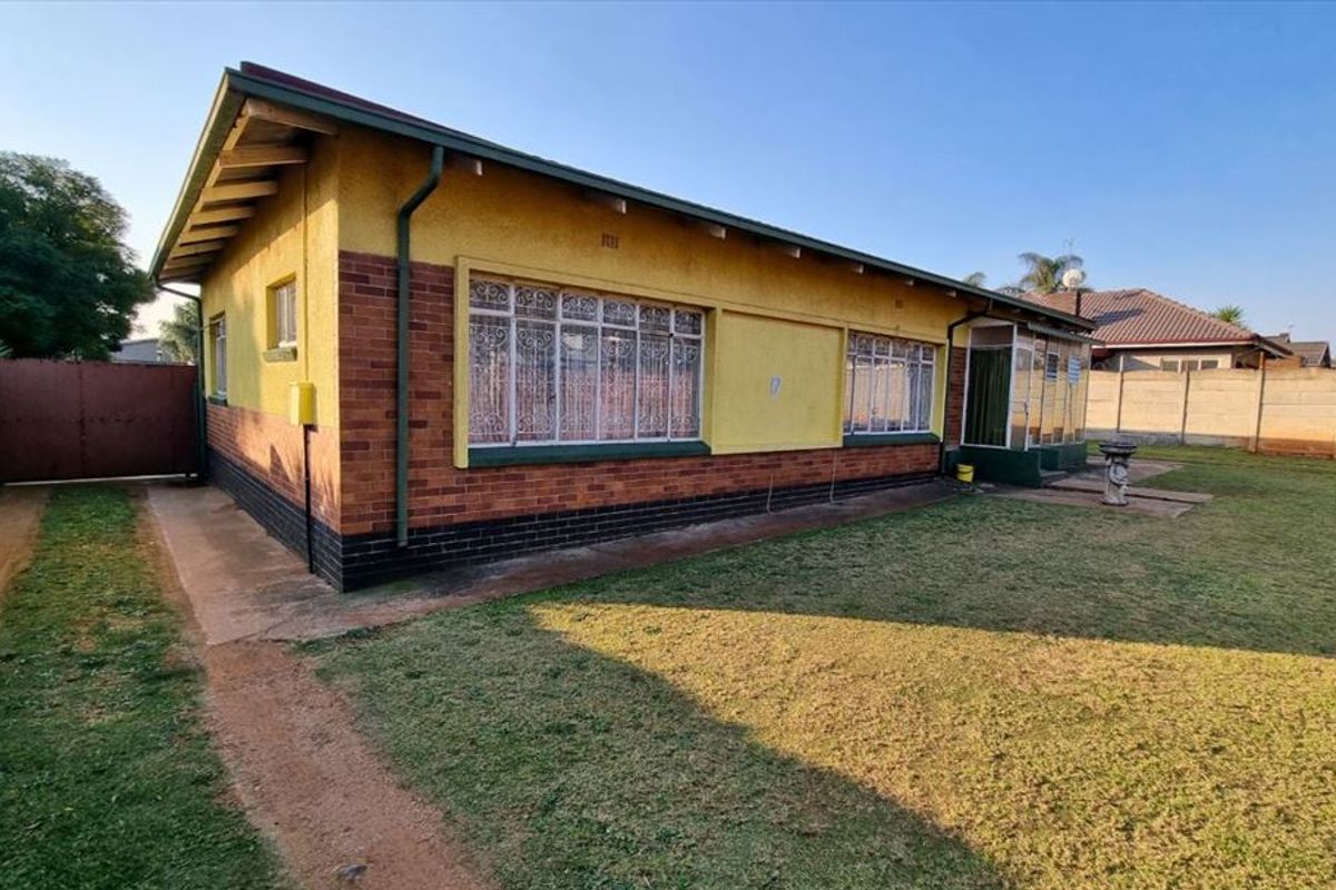 Rear view of the house featuring a combination of brick and plastered walls, security bars on windows, and a surrounding garden area.