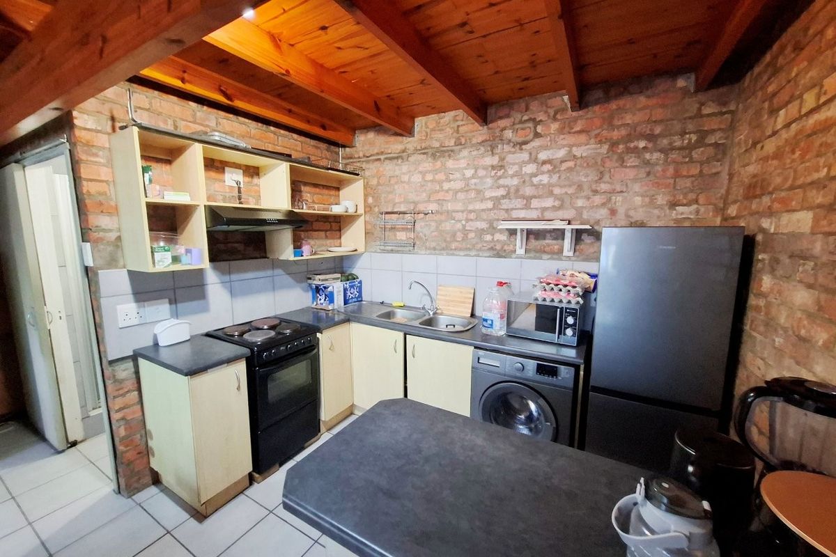 A rustic kitchen featuring exposed brick walls, timber beam ceilings, tiled flooring, and functional cabinetry with integrated sink and extractor fan.