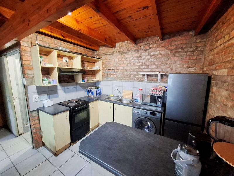 A rustic kitchen featuring exposed brick walls, timber beam ceilings, tiled flooring, and functional cabinetry with integrated sink and extractor fan.