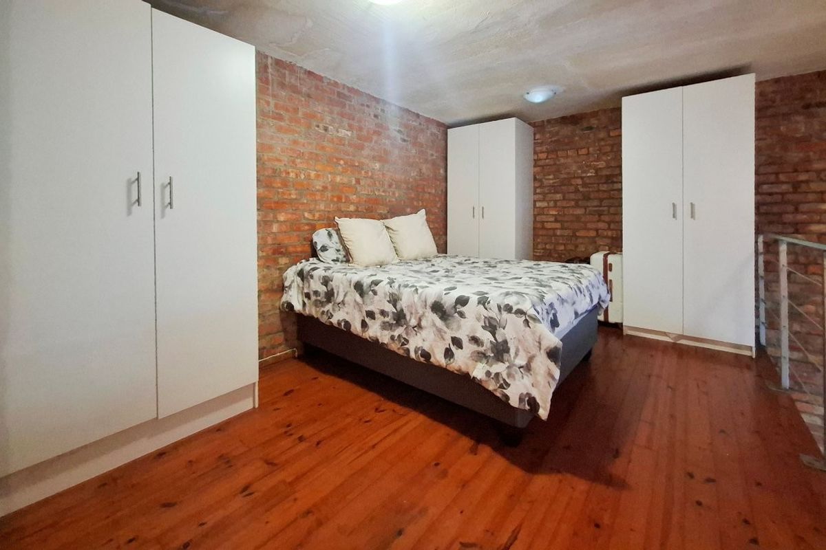 Bedroom featuring exposed brick walls, timber flooring, and multiple built-in wardrobes, situated on a mezzanine level with a metal railing.