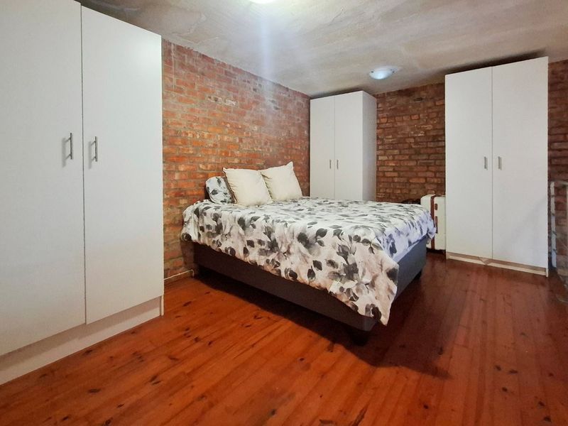 Bedroom featuring exposed brick walls, timber flooring, and multiple built-in wardrobes, situated on a mezzanine level with a metal railing.