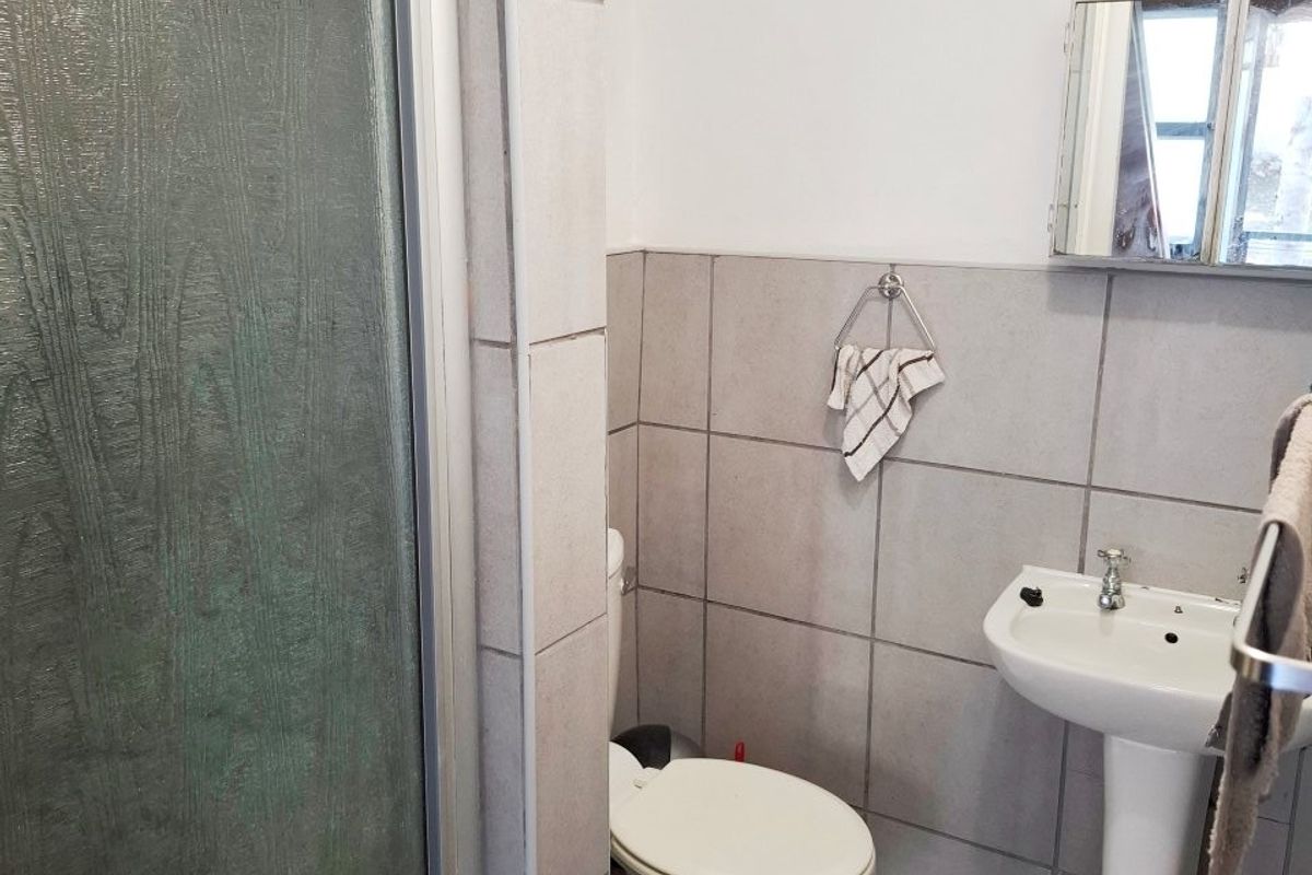 A functional bathroom featuring a pedestal basin, toilet, and a shower enclosure with tiled finishes throughout.