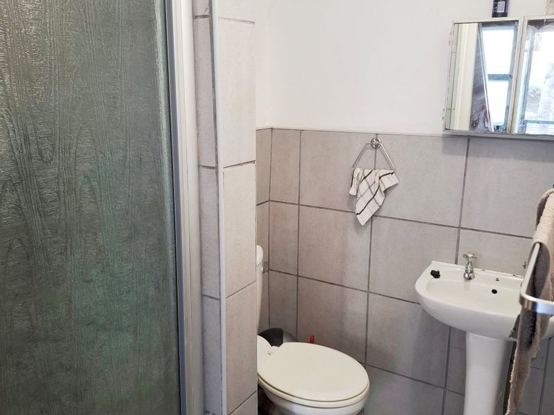 A functional bathroom featuring a pedestal basin, toilet, and a shower enclosure with tiled finishes throughout.