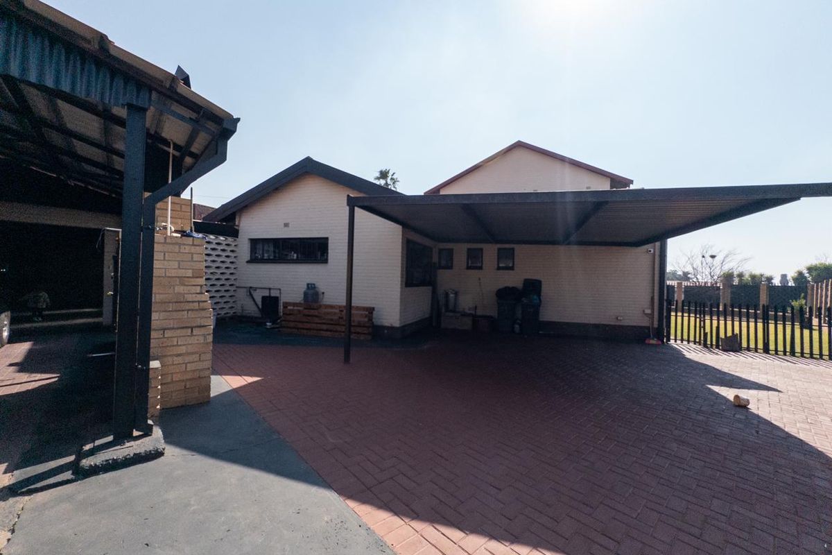 Rear exterior view featuring a paved driveway, covered carport area, and brick boundary walling.