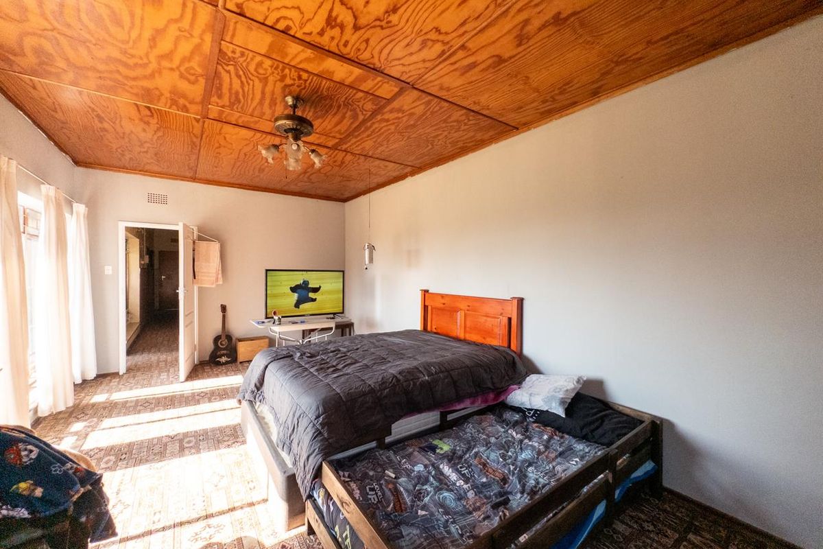 A bedroom featuring a distinctive plywood panel ceiling, ceiling fan, and carpeted flooring, offering a functional space with potential for cosmetic updates.