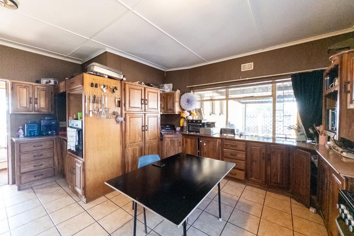 A dated kitchen featuring extensive timber cabinetry, tiled flooring, and a large window providing natural light, offering significant potential for a modern renovation.