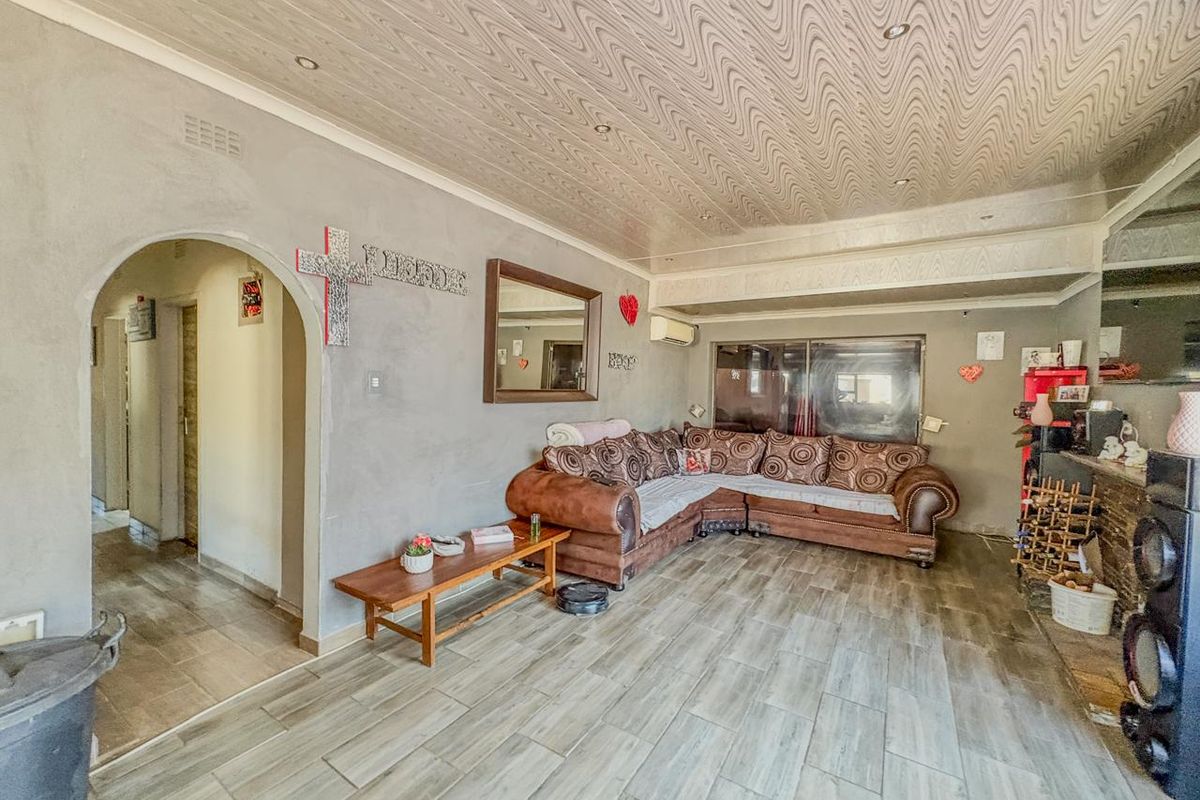 A living room featuring tiled flooring, a textured ceiling with recessed lighting, and an arched entryway leading to the hallway.