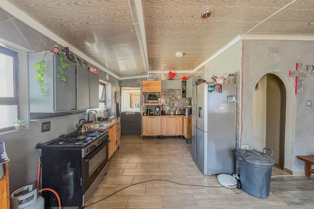 A functional kitchen featuring tiled floors, wooden cabinetry, and a gas stove, with an open archway leading to adjacent living spaces.