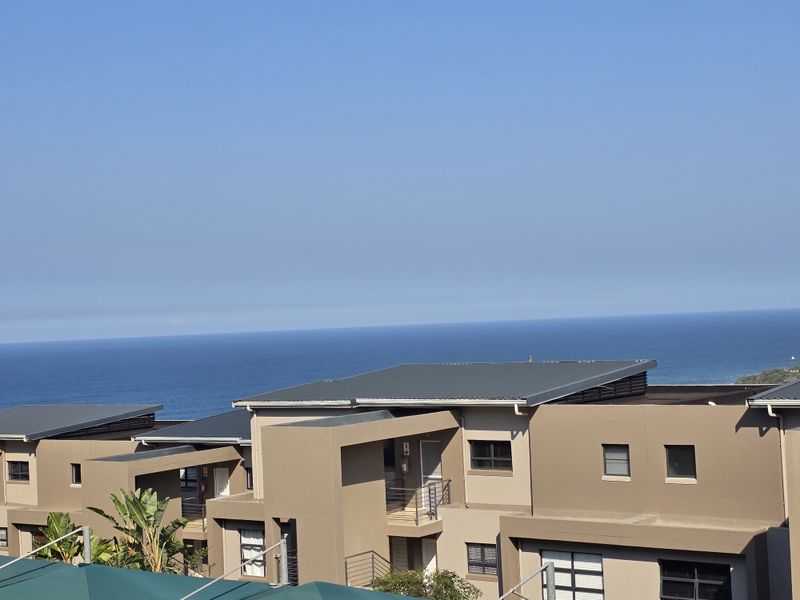 An elevated view of modern apartment building exteriors featuring contemporary architectural design, metal roofing, and a clear ocean horizon in the background.