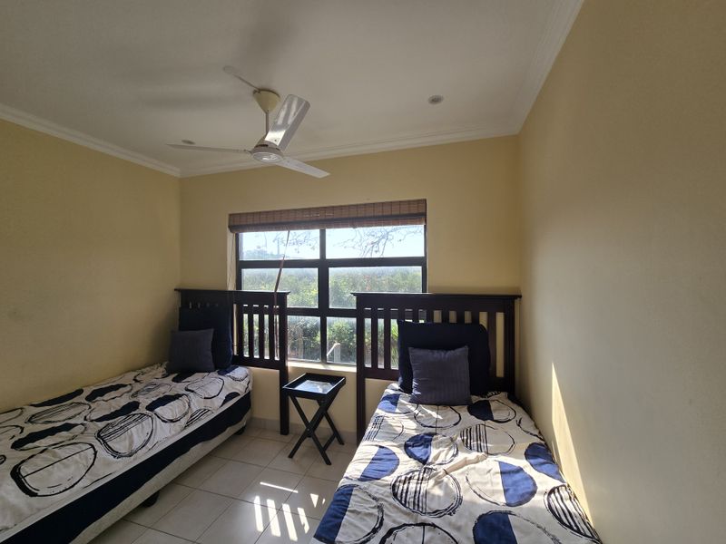 A bedroom featuring tiled flooring, a ceiling fan, and a large window with blinds, offering natural light and an exterior view.