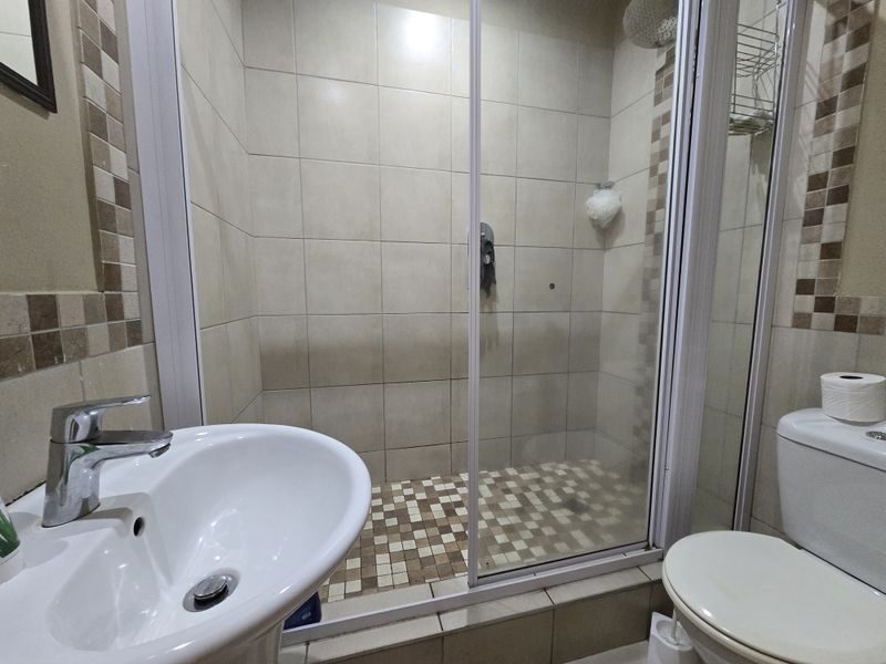 Compact bathroom featuring a pedestal basin, a tiled shower enclosure with a sliding glass door, and a standard toilet with neutral wall tiling.