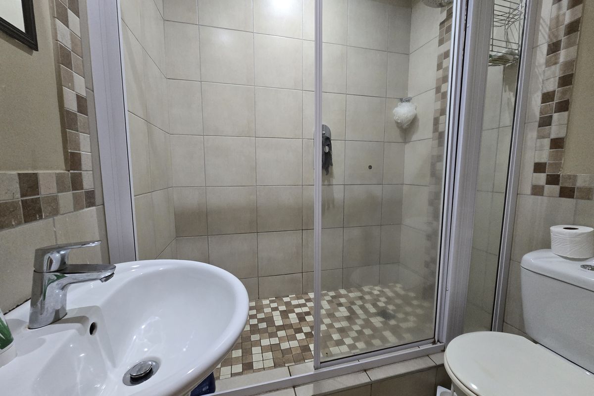 Compact bathroom featuring a pedestal basin, a tiled shower enclosure with a sliding glass door, and a standard toilet with neutral wall tiling.