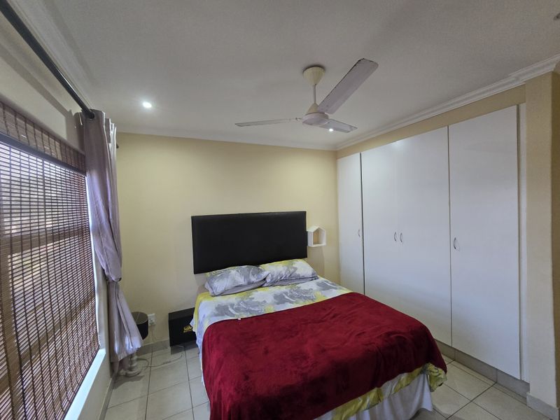 A bedroom featuring built-in white cupboards, tiled flooring, and a ceiling fan, providing a functional and neutral living space.