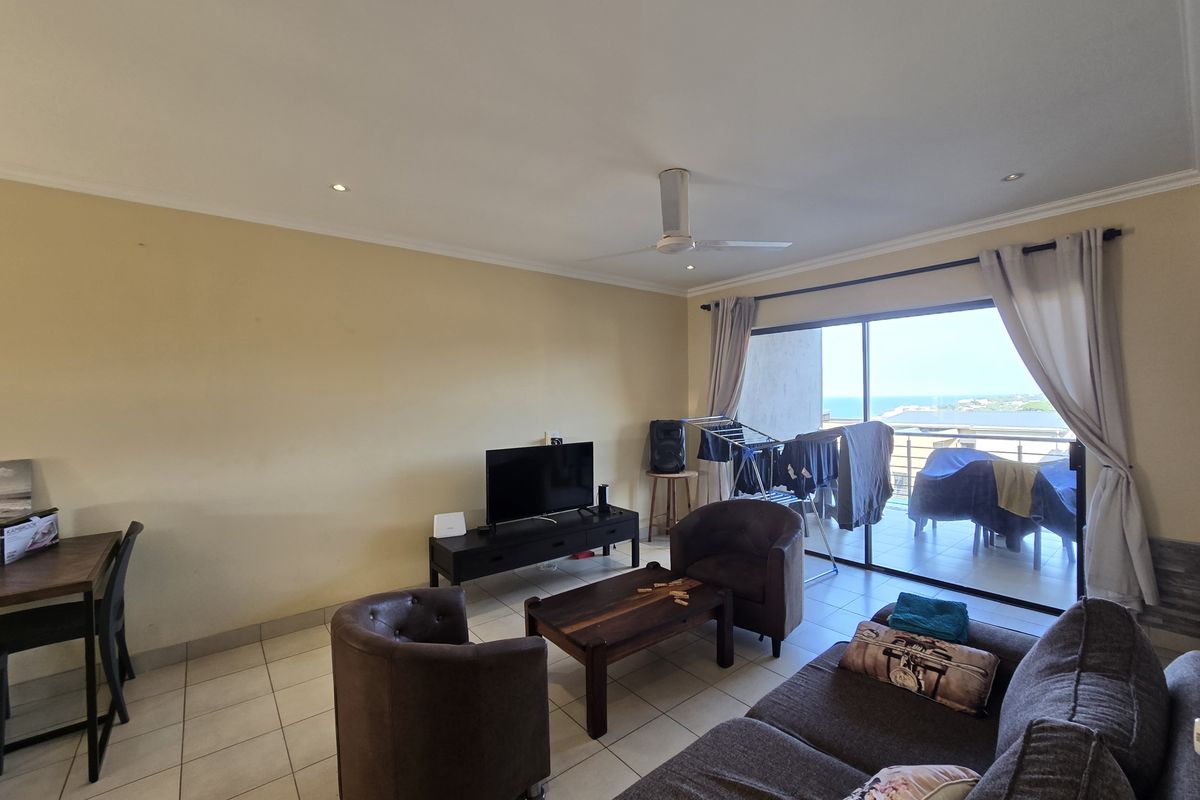 A spacious living room featuring tiled flooring, recessed lighting, and a ceiling fan, with large sliding glass doors providing access to a balcony with ocean views.