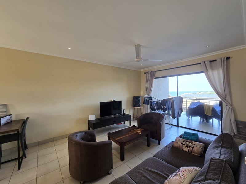 A spacious living room featuring tiled flooring, recessed lighting, and a ceiling fan, with large sliding glass doors providing access to a balcony with ocean views.
