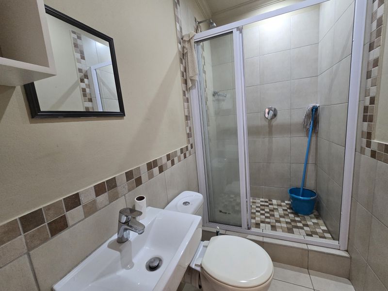 A functional bathroom featuring a shower enclosure, wall-mounted basin with mixer tap, and a standard toilet with tiled wall accents.