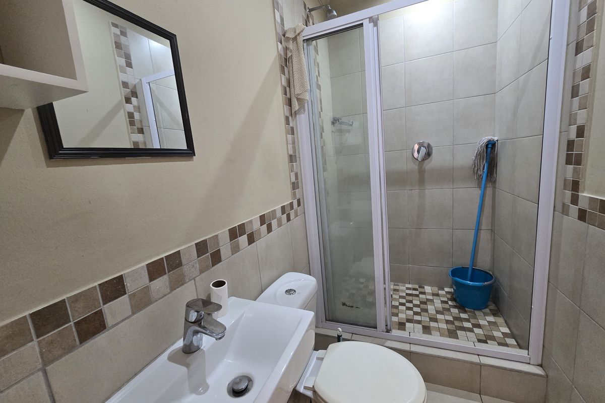 A functional bathroom featuring a shower enclosure, wall-mounted basin with mixer tap, and a standard toilet with tiled wall accents.