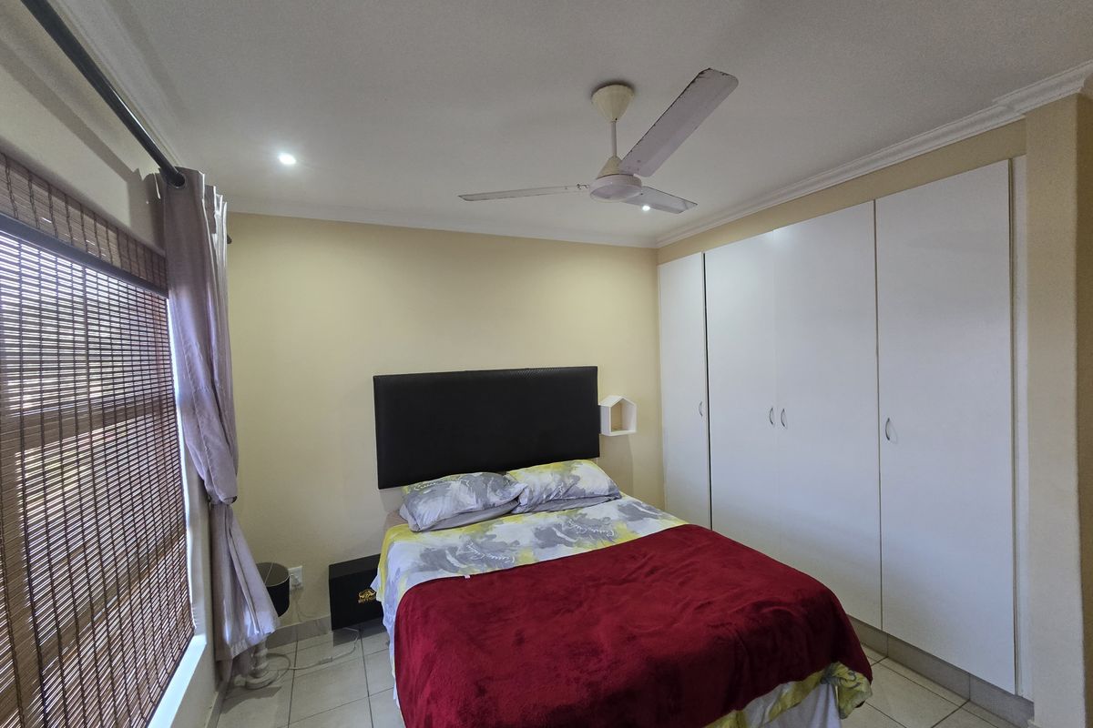 A bedroom featuring built-in white cupboards, tiled flooring, and a ceiling fan, providing a functional and neutral living space.