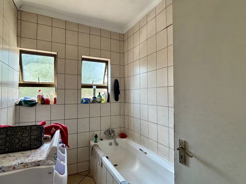 A functional bathroom featuring a built-in bathtub, tiled walls, and dual casement windows, offering a practical layout in need of cosmetic updates.