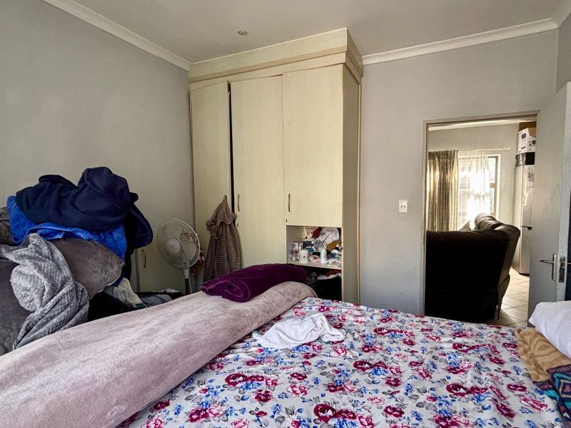 A bedroom featuring a built-in wardrobe with integrated shelving and recessed ceiling lighting, offering a functional layout with direct access to an adjacent living area.
