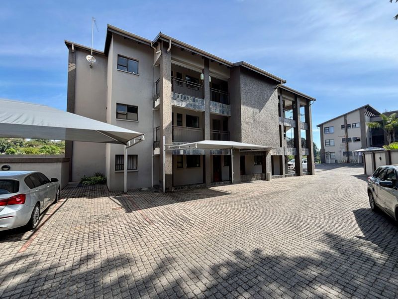 Exterior view of a multi-story apartment complex featuring paved parking areas with shade cloth carports and stone-clad balcony detailing.