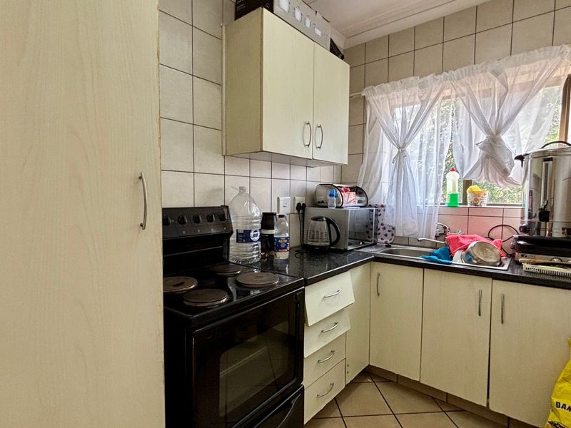 A compact kitchen featuring built-in cabinetry, tiled backsplash, and a stainless steel sink, offering a functional layout with potential for modern updates.