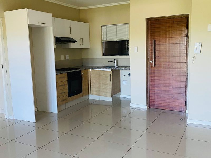 An open-plan kitchen and living area featuring tiled floors, built-in cabinetry with integrated appliances, and a solid wood entrance door.