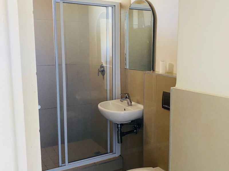 A clean, functional bathroom featuring a glass shower enclosure, wall-mounted basin, and a wall-mounted toilet with neutral tiled finishes.