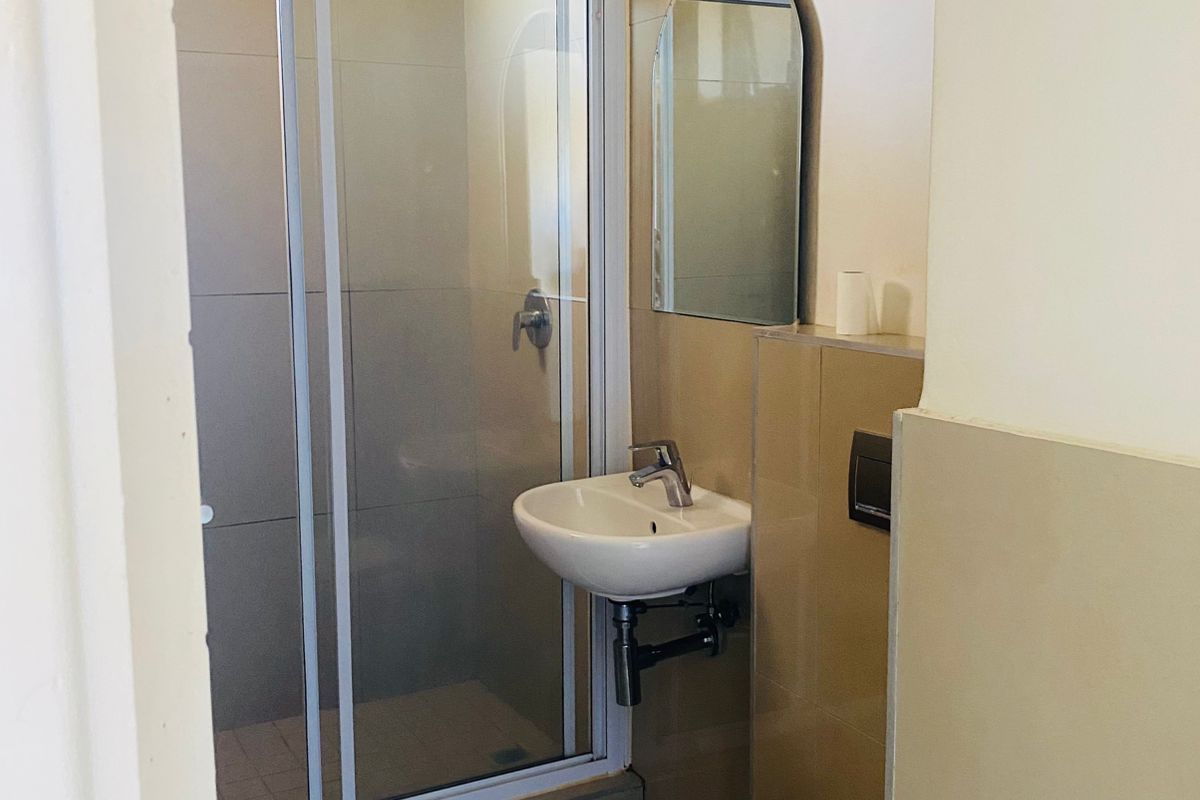 A clean, functional bathroom featuring a glass shower enclosure, wall-mounted basin, and a wall-mounted toilet with neutral tiled finishes.