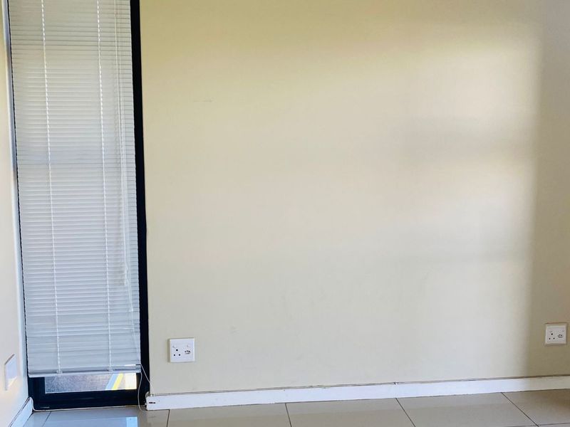 An empty bedroom featuring neutral tiled flooring, a large window with fitted venetian blinds, and standard electrical points.