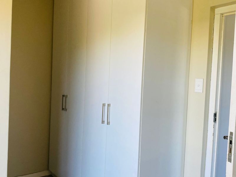 A clean bedroom area featuring white built-in cupboards, neutral wall tones, and tiled flooring, providing ample storage space.