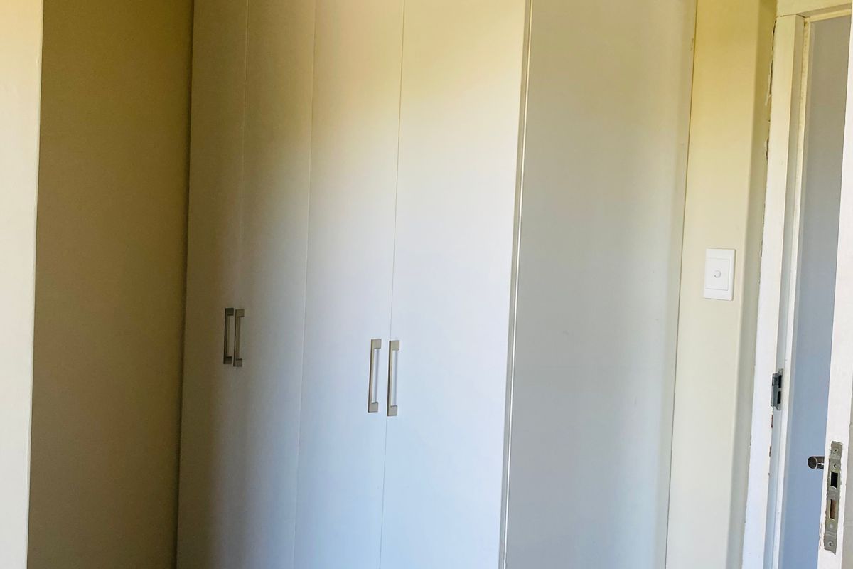 A clean bedroom area featuring white built-in cupboards, neutral wall tones, and tiled flooring, providing ample storage space.