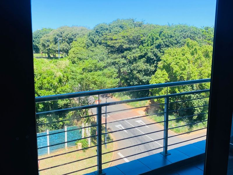 A balcony featuring tiled flooring and a stainless steel balustrade, offering an elevated view of the surrounding greenery and street.