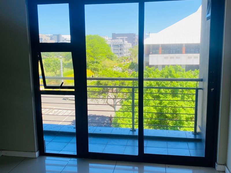 An empty room featuring large sliding glass doors that open onto a balcony with metal railings and views of the surrounding area.