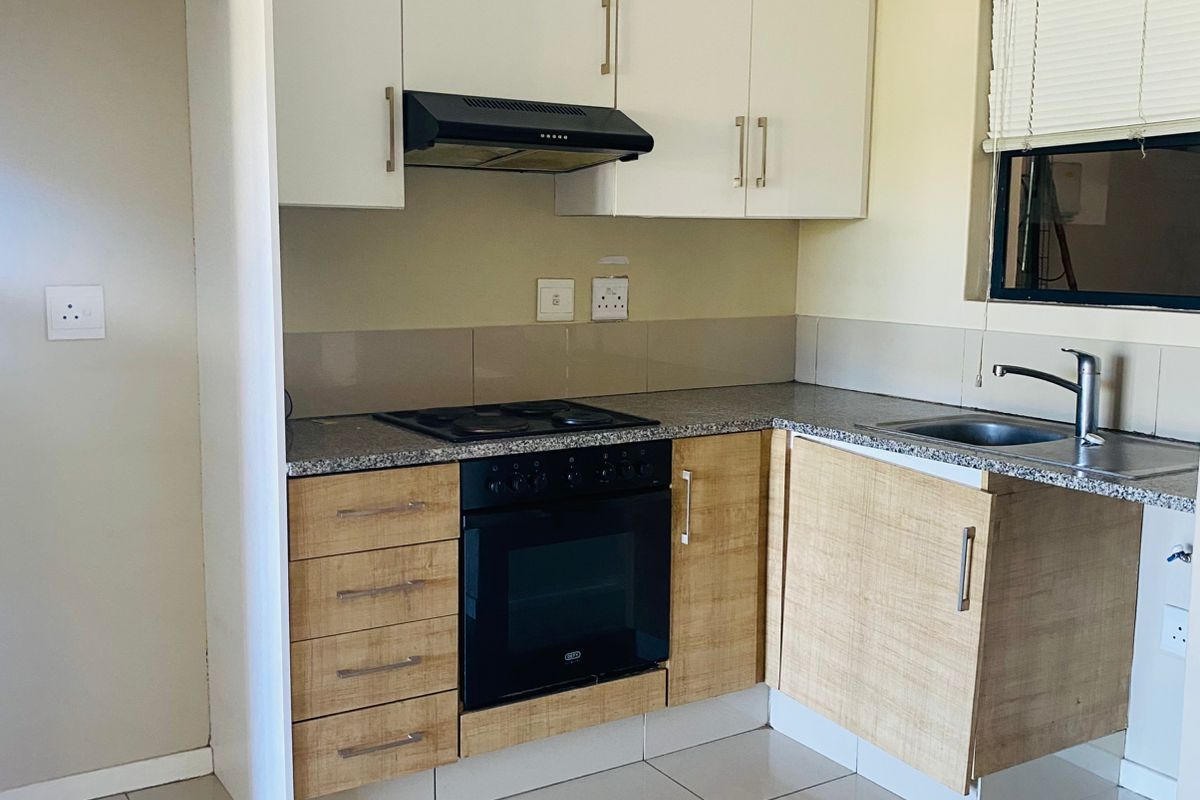 A clean, functional kitchen featuring modern two-tone cabinetry, granite countertops, built-in oven and hob, and tiled flooring.