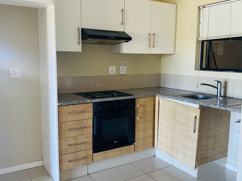 A clean, functional kitchen featuring modern two-tone cabinetry, granite countertops, built-in oven and hob, and tiled flooring.