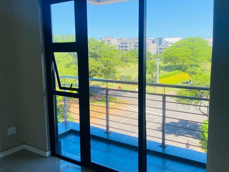 A bright, empty room featuring a large sliding glass door that opens onto a balcony with a stainless steel balustrade and pleasant neighborhood views.