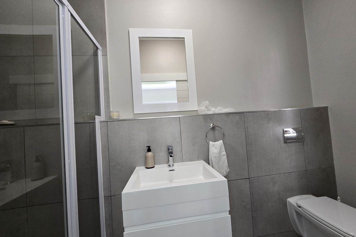Modern bathroom featuring a wall-mounted vanity, basin, wall-hung toilet, and a glass shower enclosure with contemporary grey wall tiling.