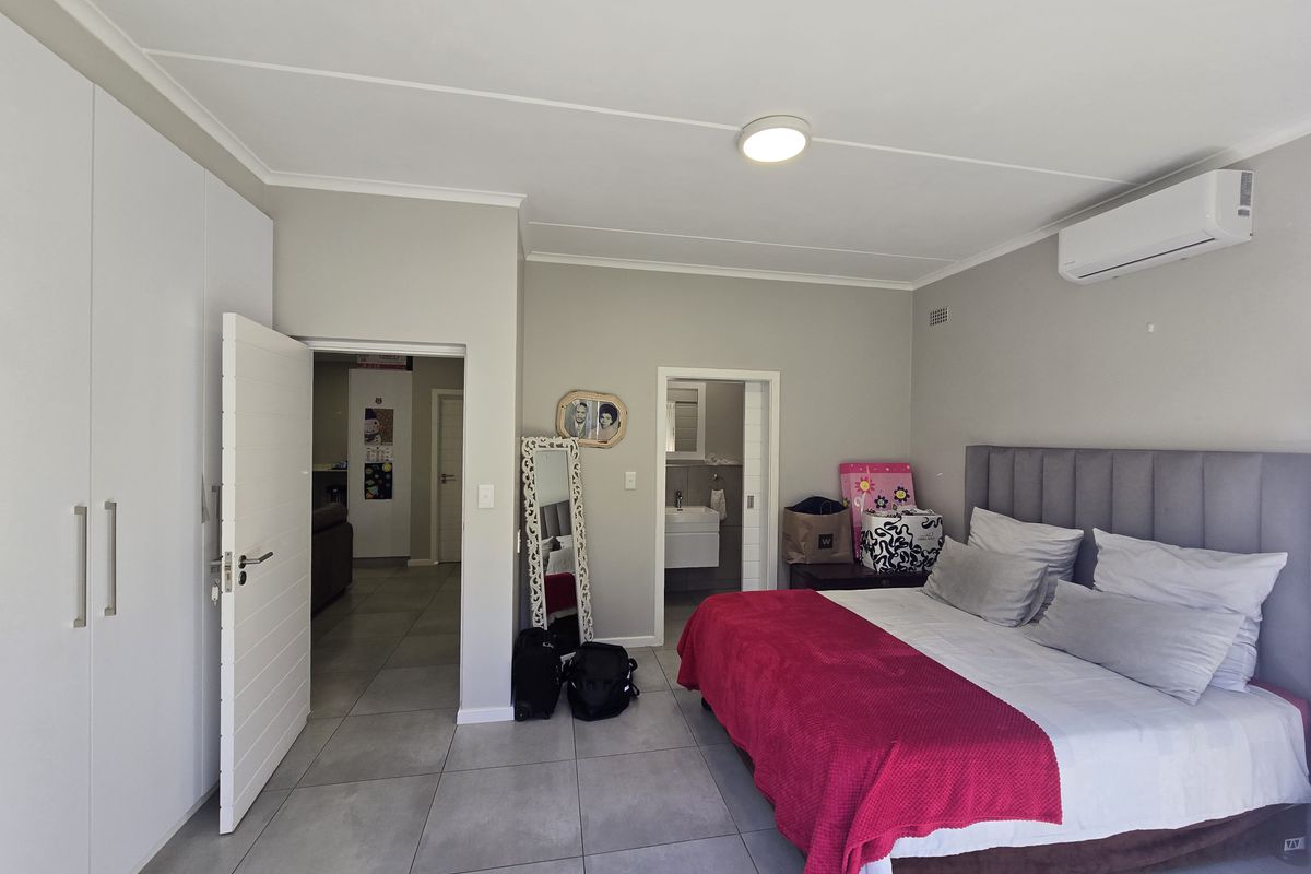 Spacious bedroom featuring neutral tiled flooring, built-in cupboards, and a wall-mounted split-system air conditioner, with direct access to an en-suite bathroom.