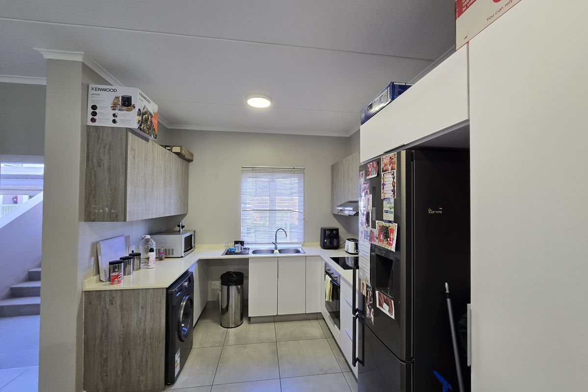 A functional kitchen featuring modern grey and white cabinetry, tiled flooring, integrated appliances, and ample counter space with a stainless steel sink.