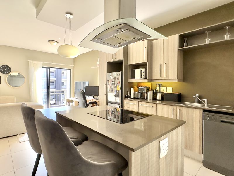 Modern open-plan kitchen and living area featuring a central island, stone countertops, integrated appliances, and direct access to a balcony.