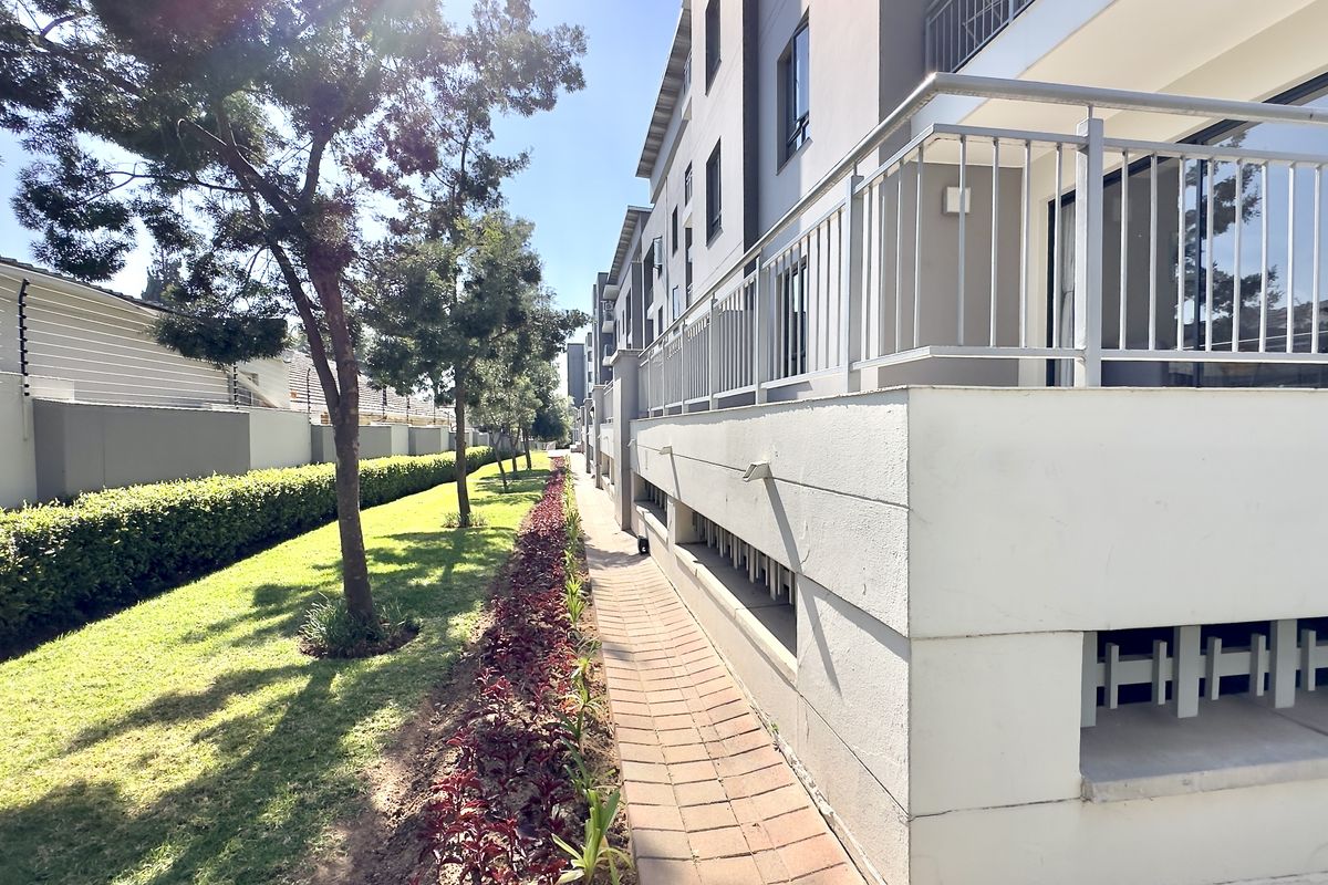 A well-maintained exterior rear view of the apartment complex featuring a paved walkway, landscaped garden, and metal balcony railings.